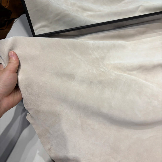 Close-up of beige fabric with a hand holding it, on a white background